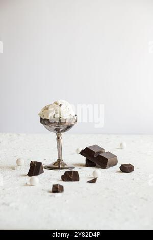 Ciotola in metallo vintage riempita con cremoso gelato alla stracciatella, decorata con pezzi di cioccolato, su uno sfondo bianco pulito per un classico bagno Foto Stock