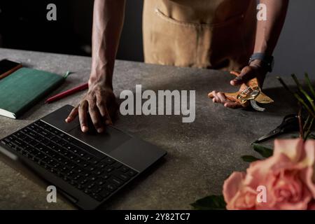 Primo piano minimale dell'irriconoscibile uomo nero come artigiano o fioraio che utilizza un computer portatile con spazio per copie dai colori scuri Foto Stock