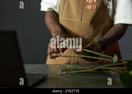 Primo piano minimale di un fioraio maschile che organizza bouquet e fusti di fiori da taglio in uno spazio fotocopie con scarsa illuminazione Foto Stock