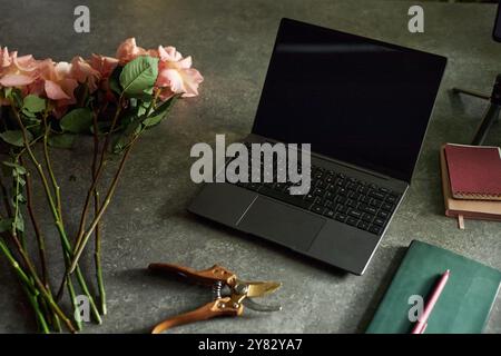 Elegante composizione dello sfondo di un laptop aperto con fiori su un tavolo scuro testurizzato in uno spazio di copia poco chiaro Foto Stock