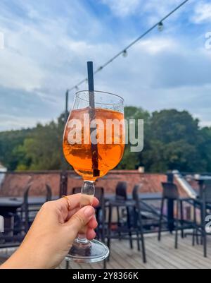 Mano femminile con anello sul dito che regge il bicchiere di cocktail Aperol spritz. Foto di alta qualità Foto Stock