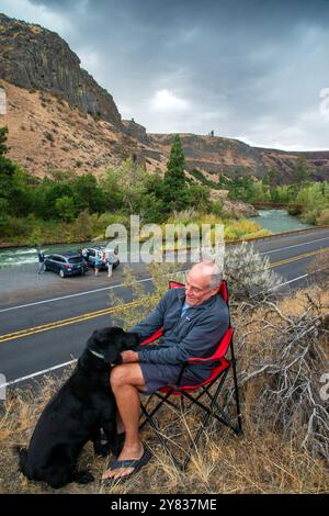 Un uomo anziano si rilassa con il suo laboratorio nero lungo l'autostrada 12 nel Tieton River Canyon fuori Yakima, Washington Foto Stock