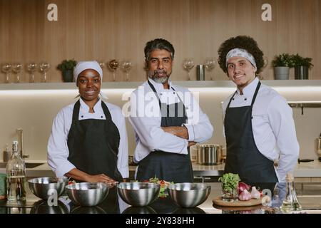Il team di cucina multirazziale sorride e guarda la fotocamera mentre posa per un ritratto insieme Foto Stock