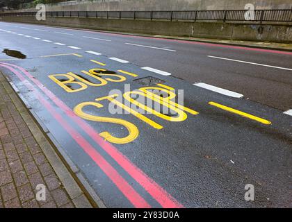 Cartello giallo della fermata dell'autobus dipinto sulla strada da una fermata dell'autobus con asfalto bagnato dalla pioggia Foto Stock