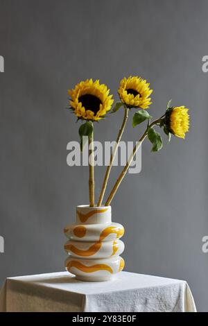 Composizione floreale minimale sui girasoli in vaso in ceramica con design retrò anni '70 su sfondo grigio semplice con accenti di colore giallo Foto Stock