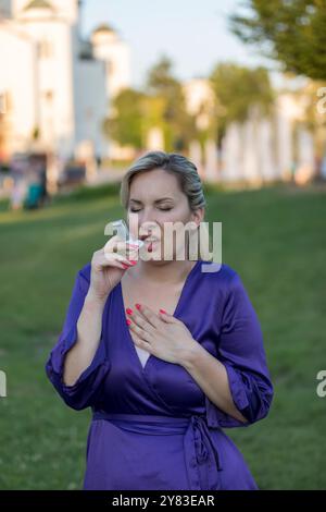 Una donna asmatica che prende un inalatore e ha un attacco d'asma. Ha un problema con l'asma e ha un inalatore. Foto Stock