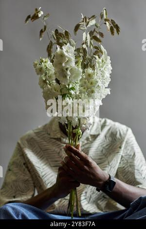 Ritratto minimale di un giovane afroamericano che tiene fiori esotici e nasconde il volto in studio Foto Stock