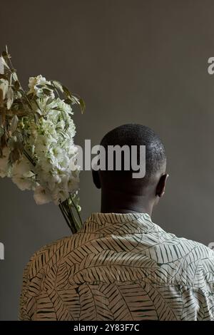 Vista posteriore minima dell'uomo afroamericano che tiene i fiori lontano dalla macchina fotografica in studio, spazio copia Foto Stock