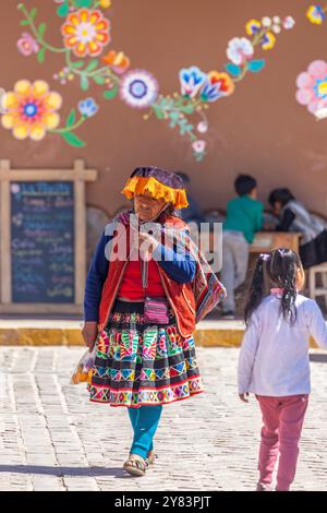 Donna quechua, con copricapo e abbigliamento tradizionali, passeggia accanto ai bambini piccoli al mercato di Pisac, in Perù Foto Stock