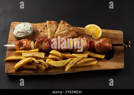 Souvlaki marinato di maiale con patate fritte, pita e salsa di yogurt su tavola di legno. Foto Stock