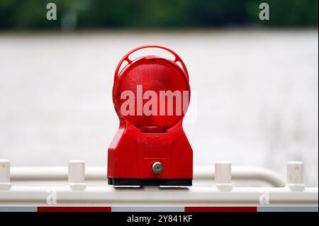 lampeggiatore di emergenza rosso su una barriera con superficie d'acqua inondata su sfondo sfocato Foto Stock