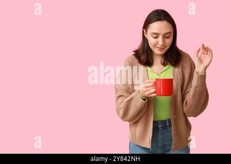 Bellissima giovane donna con una tazza di VIN brulé caldo su sfondo rosa Foto Stock