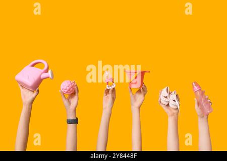 Mani femminili con accessori per bambini e giocattoli su sfondo giallo Foto Stock