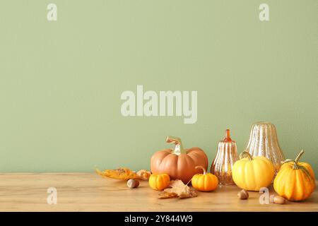 Zucche con ghiande e foglie autunnali sullo scaffale vicino alla parete verde Foto Stock