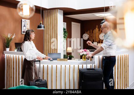 Coppia in pensione nella hall dell'hotel, chiamando per assistenza premendo il campanello del portiere mentre aspettava l'addetto alla reception. Turisti anziani, uomini e donne, con valigie che parlano alla reception, pronti per le vacanze. Foto Stock