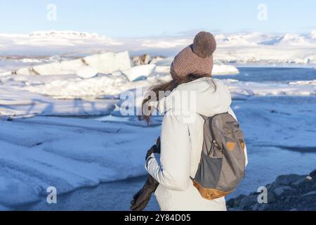 Una donna che indossa un cappotto bianco e un cappello rosa si erge su una spiaggia innevata affacciata sull'oceano Foto Stock