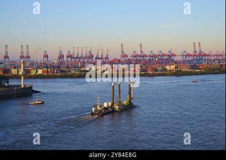 Paesaggio urbano di un porto sull'Elba, con molte gru, container, navi e turbine eoliche sotto un cielo blu in luce soffusa, alba, Amburgo, Germania Foto Stock