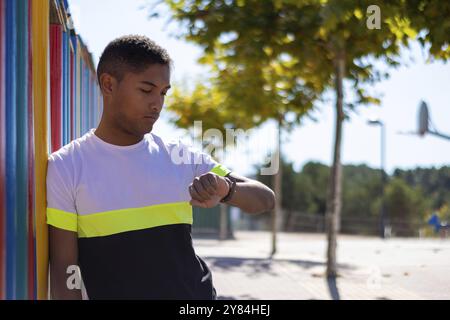 Uomo che aspetta, appoggiato su una recinzione e che guarda l'orologio, ritratto orizzontale Foto Stock