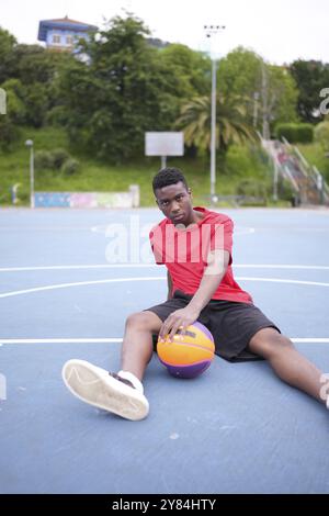 Ritratto di un giocatore di pallacanestro sportivo africano seduto in un campo all'aperto Foto Stock