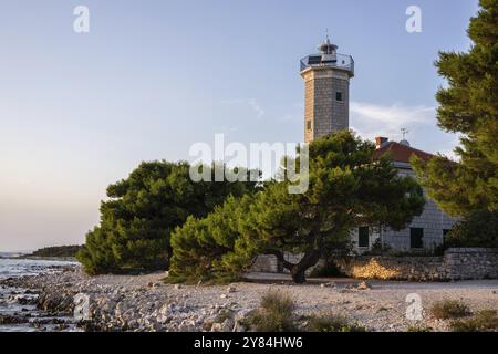 Splendido tramonto in un paesaggio su una costa rocciosa con un faro prominente e una pineta. Vista sulla costa dell'edificio, sul Mediterraneo Foto Stock