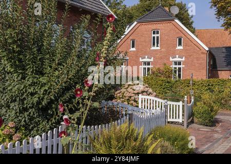 Giardino ben tenuto con fiori e recinzione bianca di fronte a una casa in mattoni in una giornata di sole, krummhoern, frisia orientale, germania Foto Stock