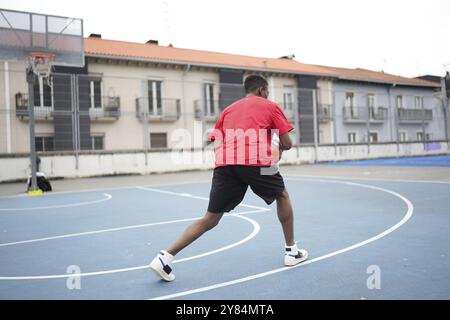 Vista posteriore di un inriconoscibile giovane afroamericano che gioca a basket all'aperto in un campo urbano Foto Stock