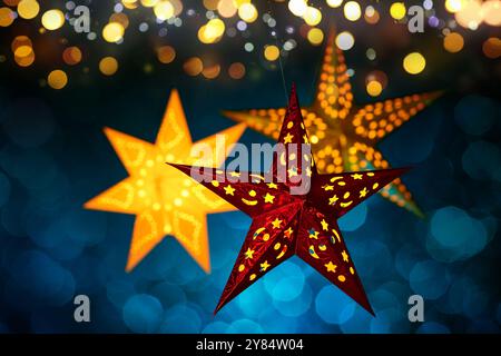 Le lanterne natalizie sono appese con luci astratte sfocate. Tre pezzi ornamentali illuminati su sfondo blu scuro con un effetto bokeh festoso Foto Stock