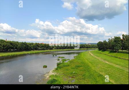 Vista panoramica estiva della città di Uzhhorod e del fiume Uzh, della Transcarpazia, Ucraina. Un fiume sereno che si snoda attraverso campi verdi sotto un cielo parzialmente nuvoloso Foto Stock