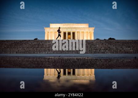 WASHINGTON DC, Stati Uniti: Un jogger solitario passa davanti al Lincoln Memorial durante le prime ore del mattino, dimostrando come questo monumento iconico serva sia come punto di riferimento storico che come spazio ricreativo urbano. L'ambientazione dell'alba evidenzia la presenza senza tempo del monumento all'estremità occidentale del National Mall. Foto Stock