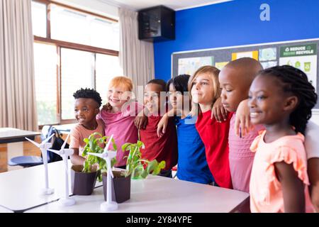 A scuola, diversi gruppi di bambini stanno insieme, sorridendo vicino alle turbine eoliche Foto Stock