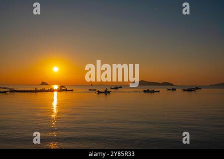 Un'alba tranquilla a Jamjindo Island, Incheon. Il sole dorato si riflette sul mare calmo, con barche da pesca che migliorano la vista serena. Foto Stock