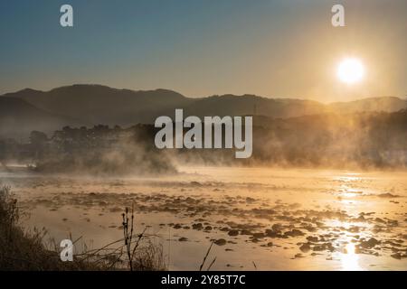 Misty mattina invernale al fiume Soyang a Chuncheon. L'alba dorata illumina la nebbia nascente, creando un paesaggio sereno. Foto Stock