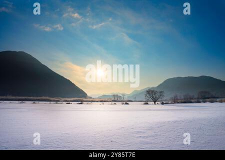 Una mattinata d'inverno su un lago ghiacciato a Jinan, Jeollabuk-do, con il sole che sorge sopra l'orizzonte, proiettando una luce dorata soffusa sulla superficie ghiacciata. Foto Stock