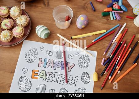 Matite colorate, pennarelli e uova decorate circondano le pagine colorate a tema pasquale creando un'atmosfera gioiosa ideale per attività creative e artigianato Foto Stock
