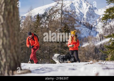 Una coppia gioca a gettare la neve al proprio cane in una giornata all'aperto tra le montagne innevate Foto Stock