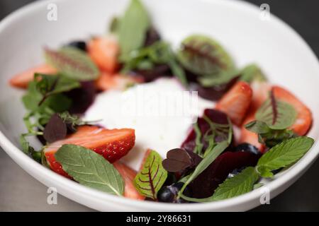 Fragole e verdure fresche servite su una cremosa base di yogurt in un recipiente bianco Foto Stock