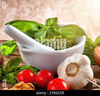 Pesto fresco in mortaio con basilico, pomodori, aglio e noci su un tavolo rustico in legno Foto Stock