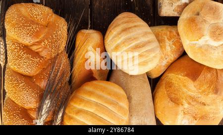 Una varietà di pane appena sfornato è disposta su un rustico tavolo in legno, accompagnato da gambi di grano Foto Stock