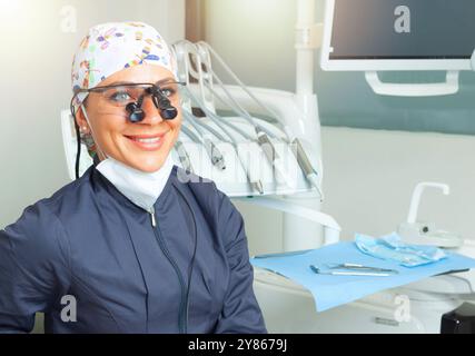 Donna sorridente dentista in un ufficio ben attrezzato circondato da strumenti dentali, trasudando professionalità e cura per la salute orale dei pazienti. Luminoso, pulito Foto Stock