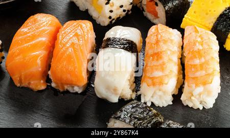 Primo piano di molti tipi diversi di sushi nigiri seduti su una superficie di ardesia nera Foto Stock