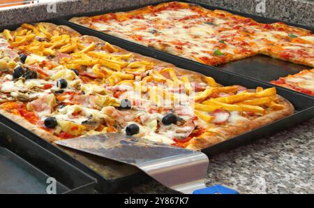 Pizze appena sfornate con mozzarella fusa e vari condimenti sono in attesa di essere servite in una pizzeria Foto Stock