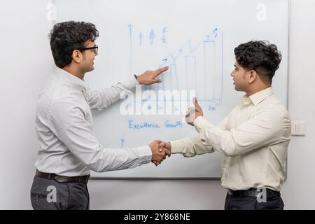 Due colleghi aziendali analizzano una strategia di crescita visualizzata su una lavagna in una sala riunioni, promuovendo un'atmosfera positiva e motivazionale Foto Stock