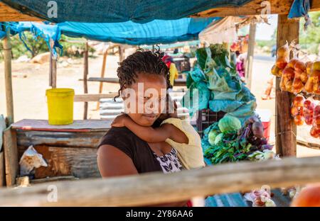 venditore ambulante africano del villaggio , madre che tiene in mano la ragazza , entrambi con capelli intrecciati, Foto Stock