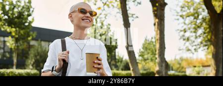 La donna sorride brillantemente mentre tiene in mano una tazza di caffè, vestita elegantemente in mezzo al verde. Foto Stock