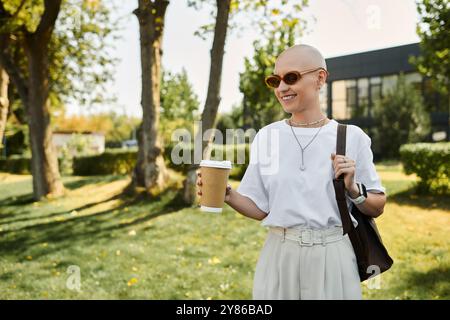 La giovane donna con un abbigliamento elegante passeggia piacevolmente attraverso un parco vivace, assaporando il suo drink. Foto Stock