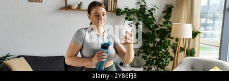 Una donna giovane e sportiva in abbigliamento attivo scatta un selfie durante l'allenamento domestico in un accogliente salotto. Foto Stock