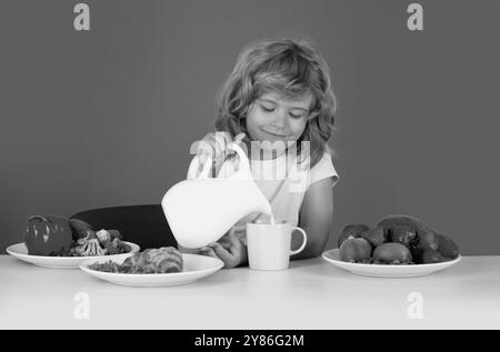 Capretto che versa latte intero di mucche. Ritratto di bambino mangiare cibo fresco sano in cucina a casa. Bambino che mangia la colazione prima della scuola. Foto Stock