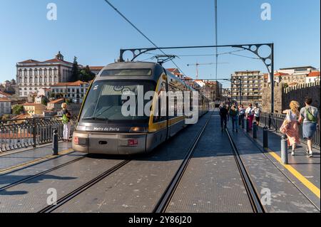 Porto, Portogallo - 12 settembre 2024: Un moderno tram arriva alla piattaforma del ponte Dom Luis i mentre i passeggeri attendono. Foto Stock