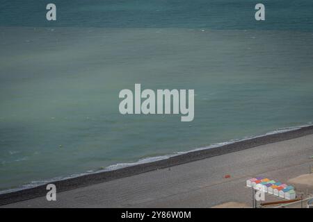 Le Treport, Francia - 09 16 2024: Vista delle cabine bianche sulla spiaggia con tetti colorati, sentieri in legno, spiaggia di ciottoli, mare blu e cielo nuvoloso dalla cima Foto Stock