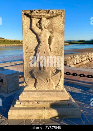 Sole serale su una scultura in pietra di una donna che bilancia un cesto pieno di pesce sulla testa vicino al porto di pescatori di Suances Cantabria Spagna Europa Foto Stock